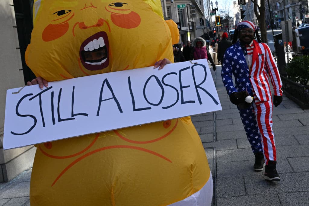 Una persona con un 
<b>disfraz inflable sostiene un cartel que dice "SIGUE SIENDO UN PERDEDOR"</b> después de la investidura del presidente estadounidense Donald Trump el 20 de enero de 2025 en Washington, DC.