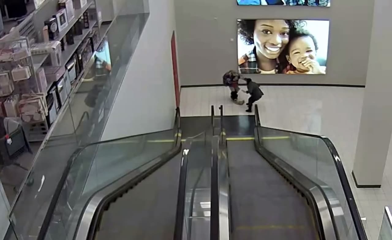 El hombre baja las escaleras eléctricas y trata de robar el bolso de una mujer. Más adelante sale de la tienda por un minuto y medio aproximadamente.