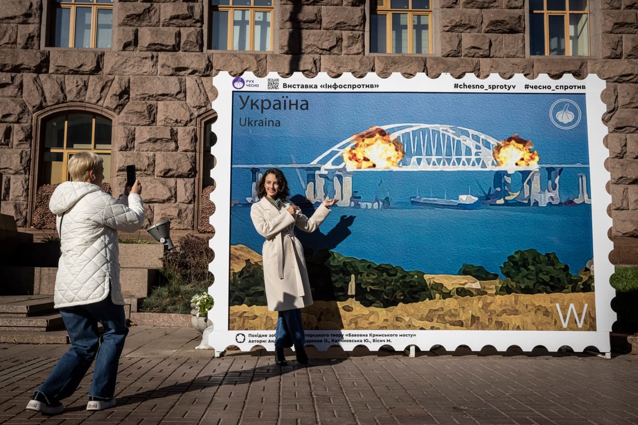 La gente posaba para fotografías frente a una imagen de un sello postal que muestra la impresión de un artista del puente de Kerch en llamas, el 8 de octubre de 2022 en el centro de Kiev, Ucrania. 
<br>
<br>
<b>Putin fue informado sobre la explosión. </b>El líder parlamentario del partido del 
<a href="https://www.univision.com/temas/volodymyr-zelensky">presidente ucraniano Volodymyr Zelensky </a>no llegó a afirmar el sábado que Kiev era el responsable, pero dijo: "La construcción ilegal rusa está comenzando a desmoronarse... 
<b>la razón es simple: si construyes algo explosivo, tarde o temprano explotará”, </b>escribió en la red social Telegram David Arakhamia.
<b> </b> 
<br>
<br>