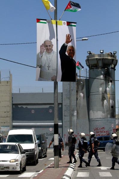 Fuerzas de seguridad palestinas pasan junto a una pancarta gigante con los rostros de Mahmud Abbás y el papa Francisco.