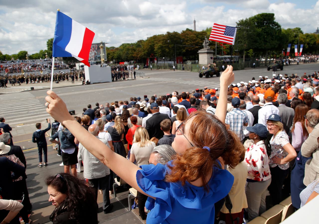 Una de las asistentes al desfile en las gradas ondea las banderas de Francia y de Estados Unidos.