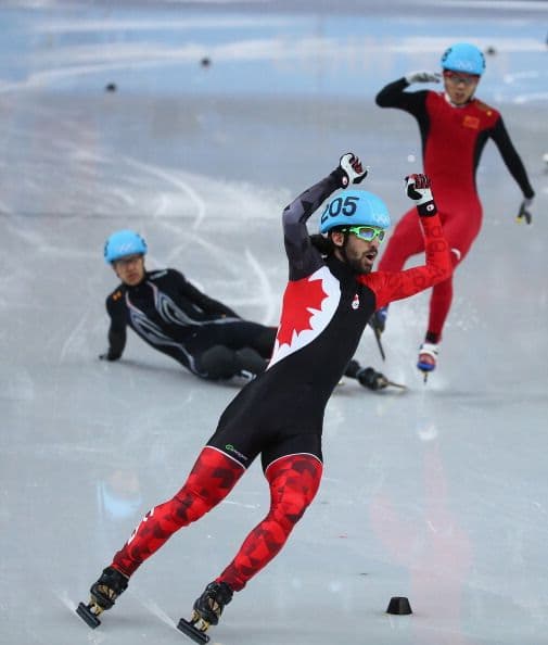 Charles Hamelin, de Canadá, celebra mientras otro de los competidores de la prueba de 1500 metros cae en la pista.