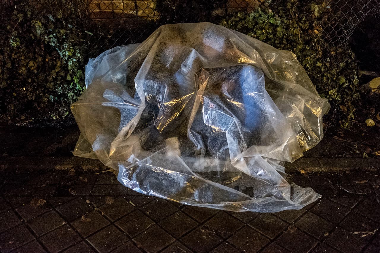 A mother and child from Colombia await their opportunity to file an asylum application in Madrid. Forced to sleep in the street, they take cover from the rain under a plastic sheet.