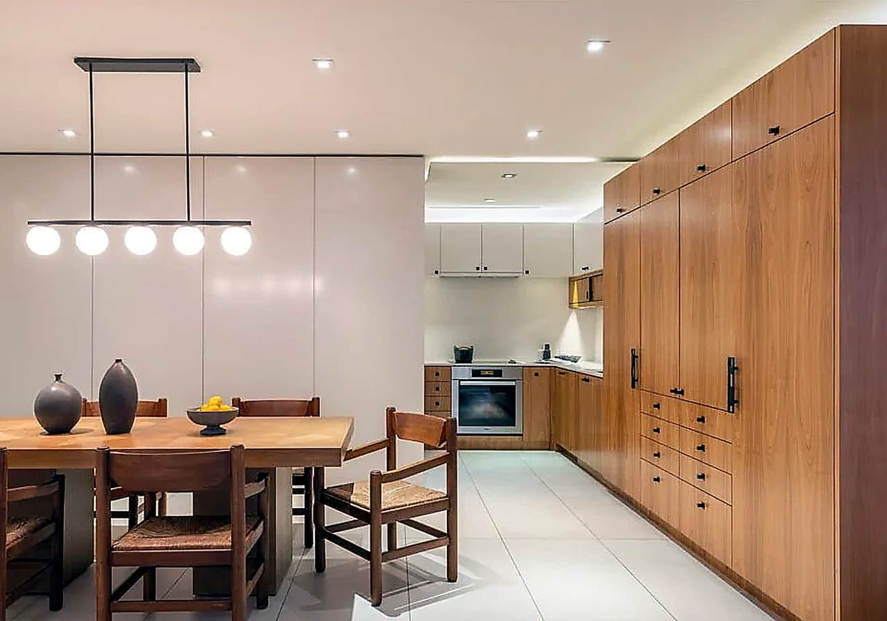 El apartamento cuenta con un espacioso comedor donde las paredes y el techo blanco resaltan el color natural de la mesa y gabinetes de madera.