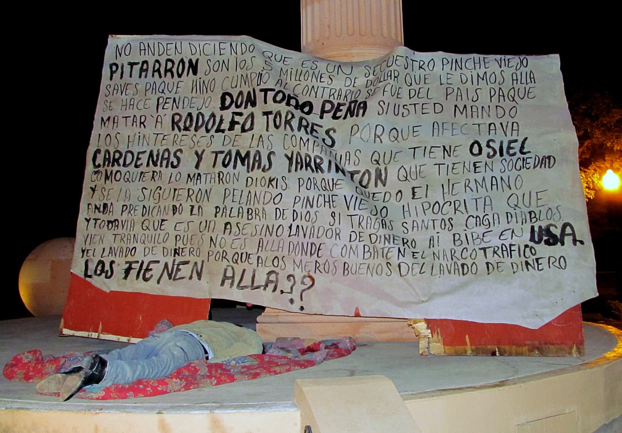 El cuerpo de un hombre junto a 'narcomanta' dejados en noviembre de 2011 en el monumento a Cristóbal Colón en Nuevo Laredo.