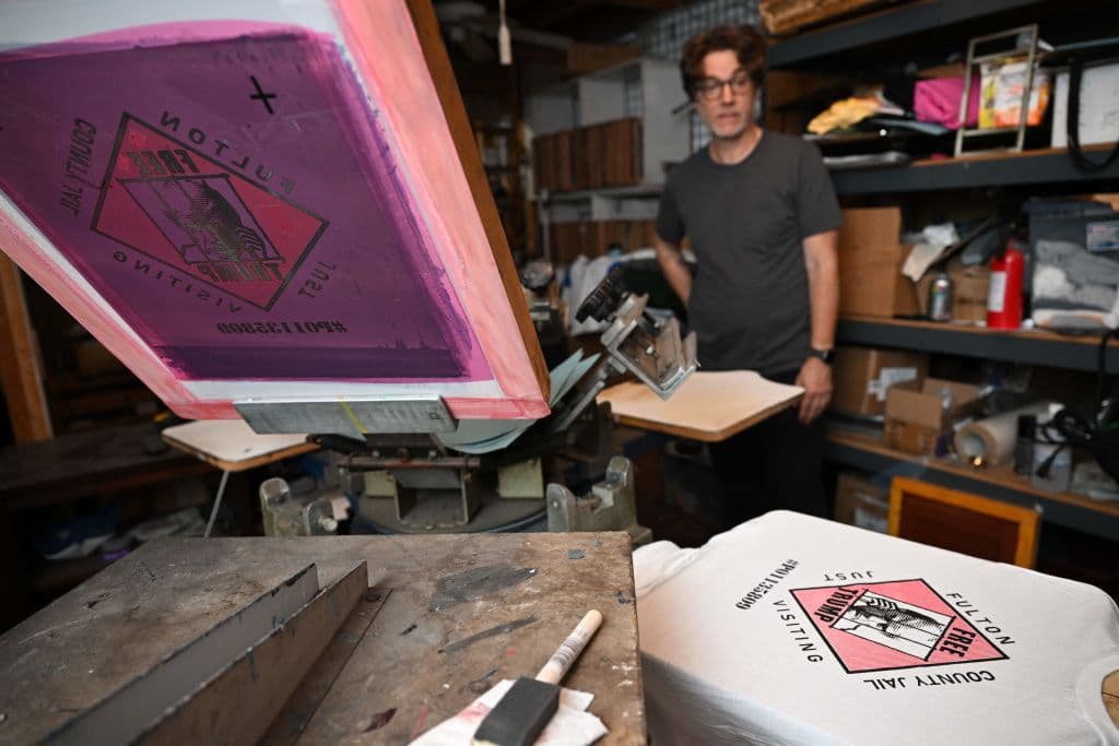 Todd Moss, quien imprime en Y-Que los diseños exclusivos en los que colocan la histórica foto del expresidente Trump, trabajaba este miércoles 30 de agosto con este. Su mensaje refuerza que el icónico líder republicano solo irá de visita a la prisión de Fulton, en Georgia.