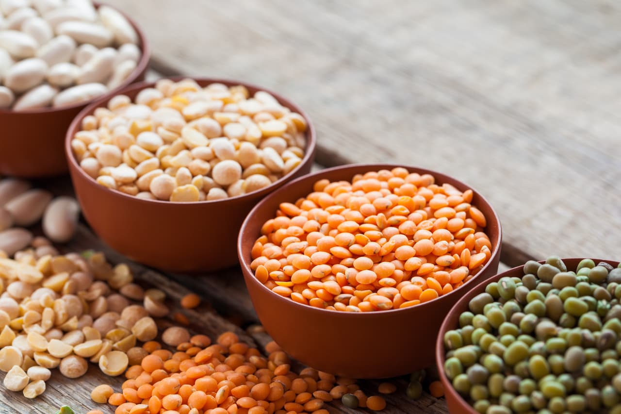 Bowls of cereal grains: red lentils, green mung, corn, beans and peas on wooden kitchen table. Selective focus.
