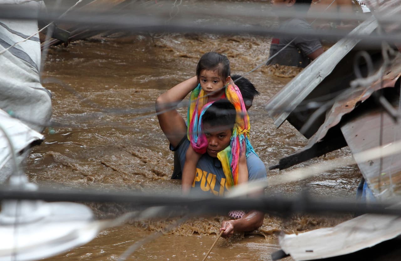 Un hombre camina con el agua cubriéndole casi por compleo el pecho mientras lleva a una niña a un sitio a salvo en una calle inundada en la ciudad de Cagayan. Policías, soldados y voluntarios trabajaban con ayuda de palas para intentar encontrar cuerpos sepultados por el lodo y los escombros en pueblos agrícolas.