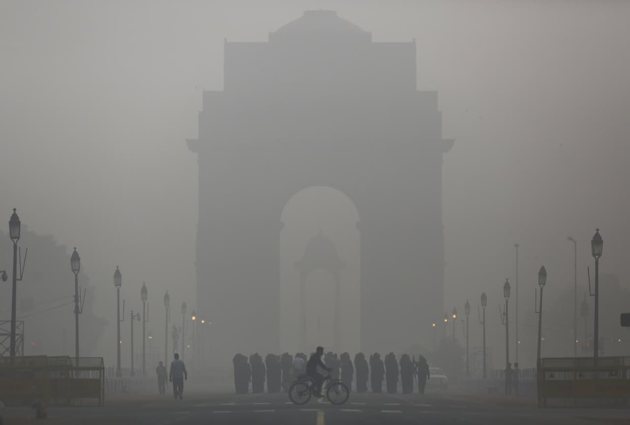 Un hombre corre bicicleta frente al puente de India en Nueva Delhi