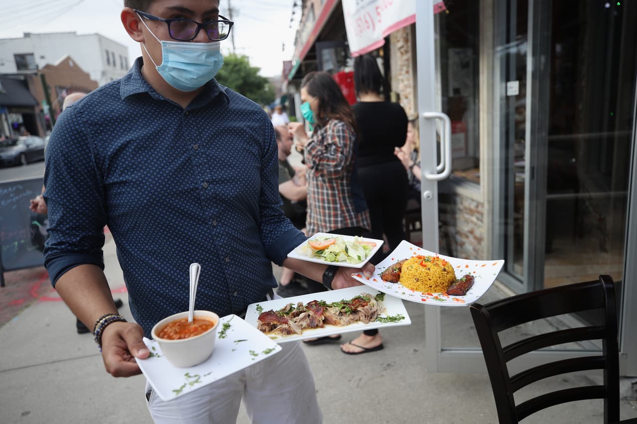 Oscar Jiménez, un mesero del restaurante dominicano 4 on Main Street en Farmingdale, Nueva York, lleva platos de comida a sus clientes usando máscara.