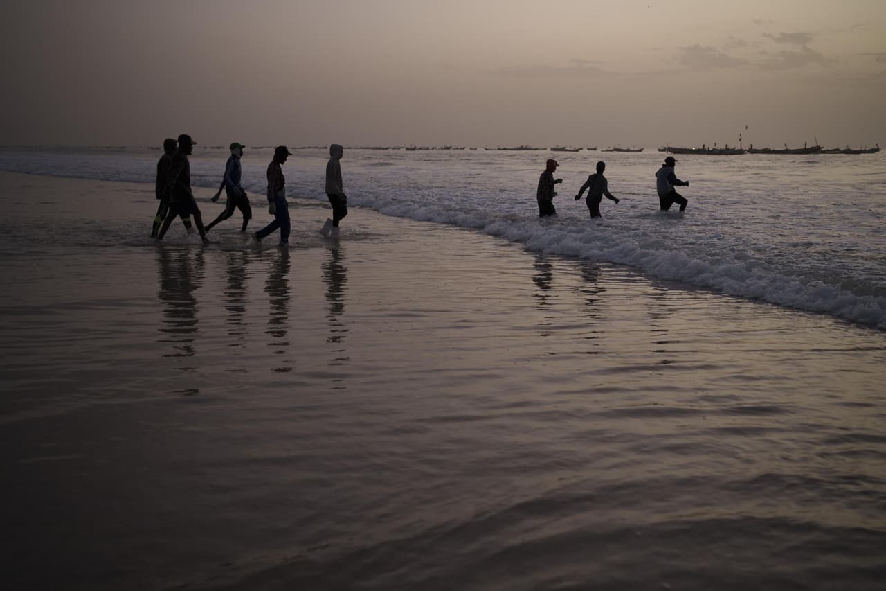Un grupo de pescadores jóvenes camina hacia el mar para subir a una embarcación tradicional de pesca, en Nuakchot, Mauritania, el 10 de diciembre de 2021.