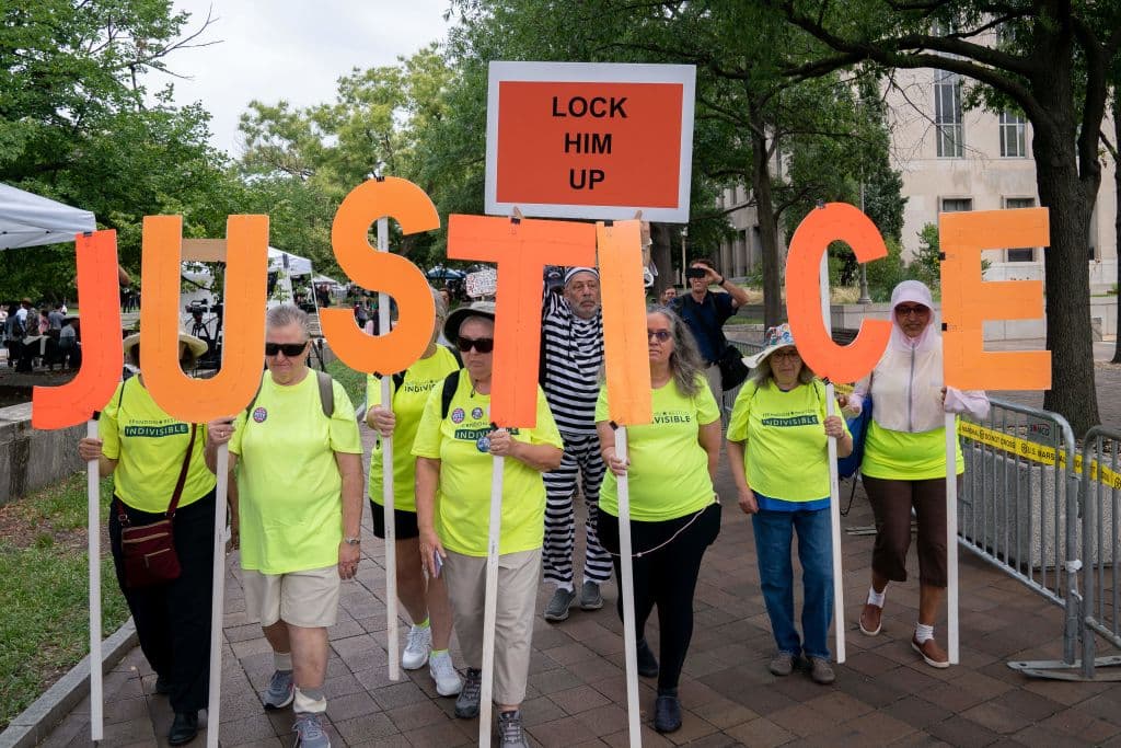 Un grupo camina hacia el edificio de la corte federal formando la palabra "justicia". Detrás un hombre vestido de presidiario alza el cartel "Enciérrenlo" que era la frase que usaban los simpatizantes del expresidente durante la campaña de 2016 contra su contrincante demócrata Hillary Clinton.