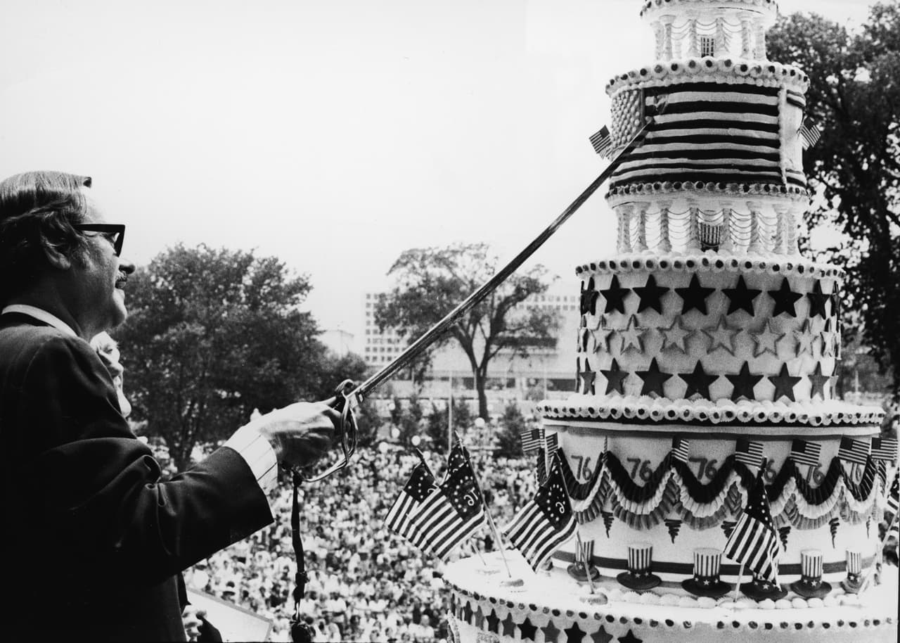 <b>El cuatro de julio en la pandemia</b>
<br>
<br>Por segundo año consecutivo el tradicional desfile para celebrar el día de independencia en el centro de Washington DC fue cancelado.
<br>
<br>“Se canceló el Desfile del Día de la Independencia Nacional de este año debido a limitaciones de logística y planificación. Las unidades que viajan desde todo el país para participar no han tenido los 8 a 18 meses necesarios para organizar, ensayar y recaudar fondos, y la mayoría aún no puede viajar debido a preocupaciones por el covid-19. Esperamos presentar esta celebración roja, blanca y azul del cumpleaños de Estados Unidos nuevamente el 4 de julio de 2022”,
<a href="https://july4thparade.com/"><u>se lee en el sitio web de los organizadores del desfile</u></a>.
<br>
<br>En la fotografía James B. Rhoads, archivista de los Estados Unidos, cuando cortaba un pastel para celebrar el aniversario 200 de la independencia. Fue uno de los momentos más importantes del tradicional desfile para conmemorar el cumpleaños del país en las calles de Washington DC, el cuatro de julio de 1976.
<br>