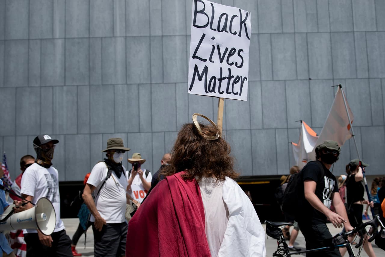 Un hombre vestido como Jesús observa a los manifestantes del movimiento 
<i>Black Lives Matter</i>. En la víspera, 
<a href="https://www.univision.com/noticias/elecciones-en-eeuu-2020/trump-amenaza-a-los-manifestantes-que-planean-ir-a-su-mitin-de-relanzamiento-de-campana-en-tulsa">Trump había advertido</a> que quienes protestaran allí serían tratados con dureza. “Cualquier manifestante, anarquista, agitador, saqueador o escoria que vaya a Oklahoma, por favor, comprenda que no lo tratarán como si hubiera estado en Nueva York, Seattle o Minneapolis. ¡Será una escena muy diferente!”, dijo en 
<a href="https://twitter.com/realDonaldTrump/status/1273972301156016130" target="_blank">un tuit.</a>