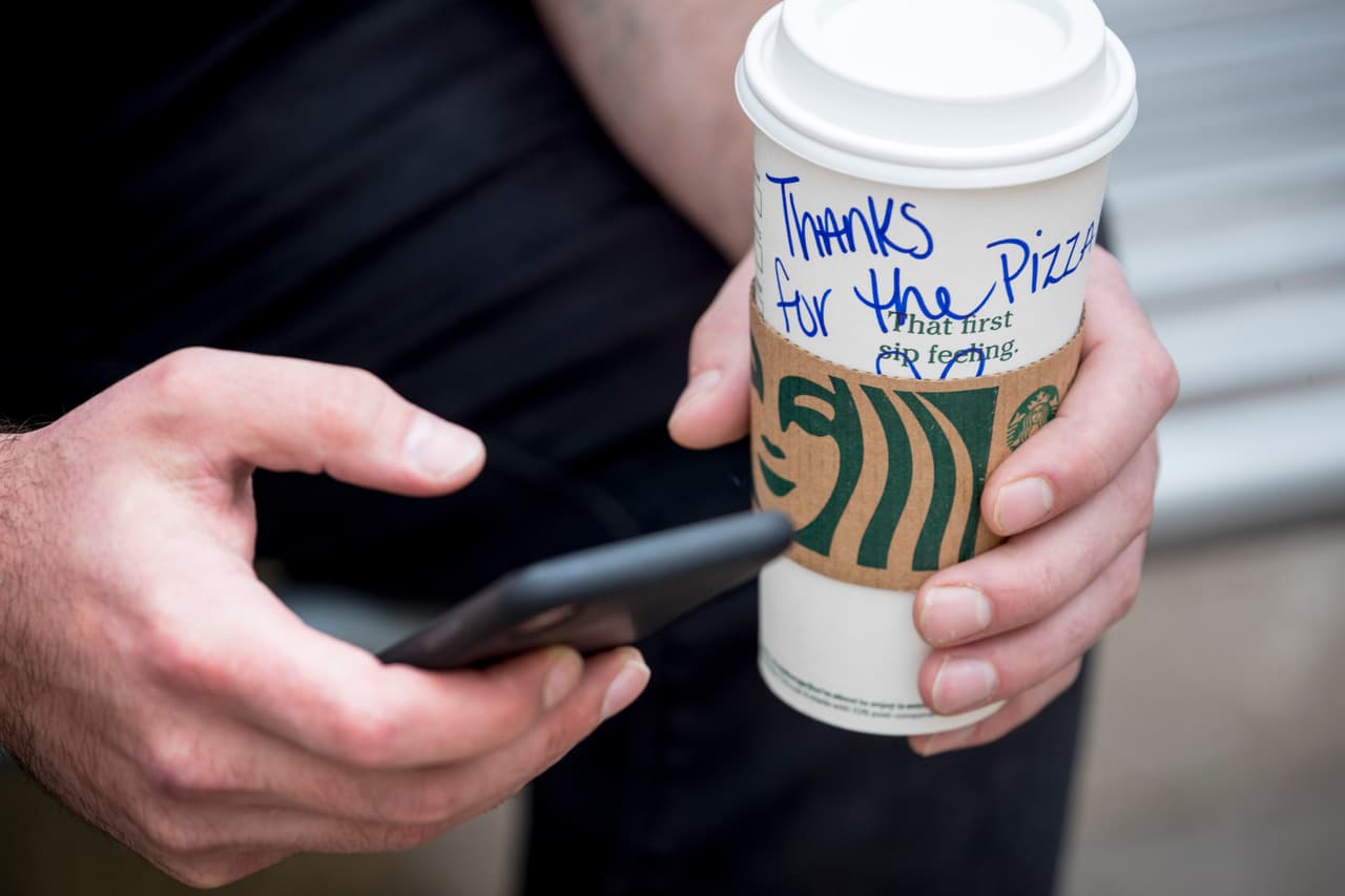 Un empleado de una pizzería sostiene un vaso de café donde se lee "¡Gracias por la pizza!", frente a un hospital de Washington DC. El restaurante ‘&pizza’ ha entregado comida gratis a los empleados de ese hospital durante varias semanas.