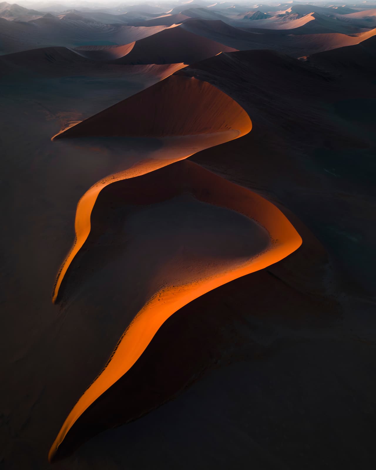 El desierto del Namib, antiguo e implacable, lleva la luz del amanecer como una corona. A medida que sale el sol, se revela esta obra maestra.
<br>