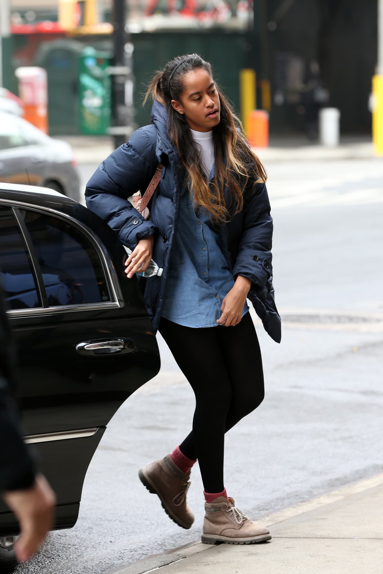 Malia Obama usa una camisa larga de jean, botas, chamarra para la nieve, medias cortas rojas y medias veladas.