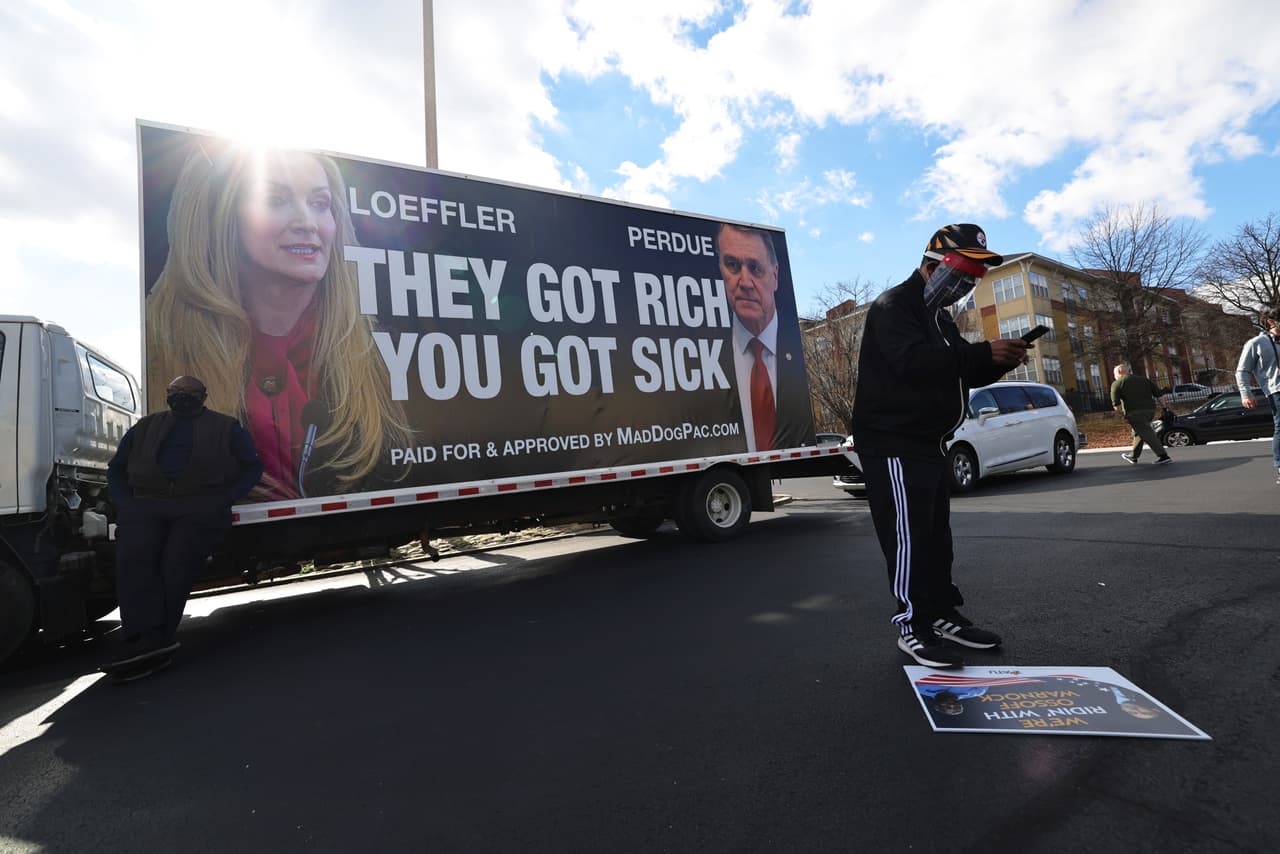 Un hombre mira su teléfono frente a un anuncio político en un lugar que sería visitado por el candidato demócrata de Georgia, el reverendo Raphael Warnock, en IBEW Local 613 este 5 de enero de 2021 en Marietta, Georgia.