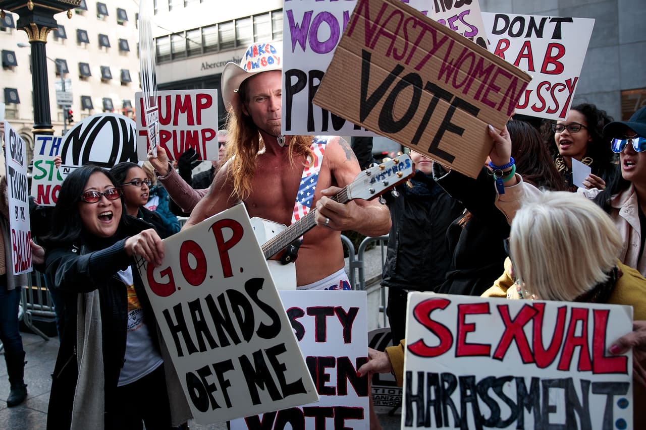 Con sus pancartas, las seguidoras de Hillary Clinton casi taparon al Vaquero desnudo pro Trump.