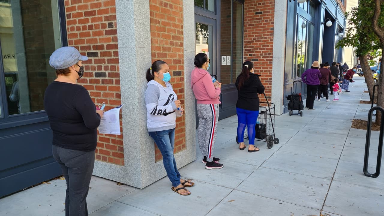 Mientras esperan su turno para recibir comida, personas apartan su lugar y tienen la oportunidad de hablar de temas de salud y el coronavirus con miembros de 'Street Team'.