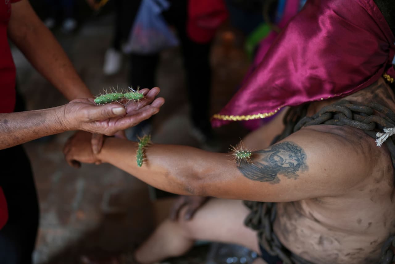 Un penitente enmascarado extiende un brazo para que le coloquen cactus antes de participar en una procesión el Viernes Santo, 18 de abril de 2025, en Atlixco, México.