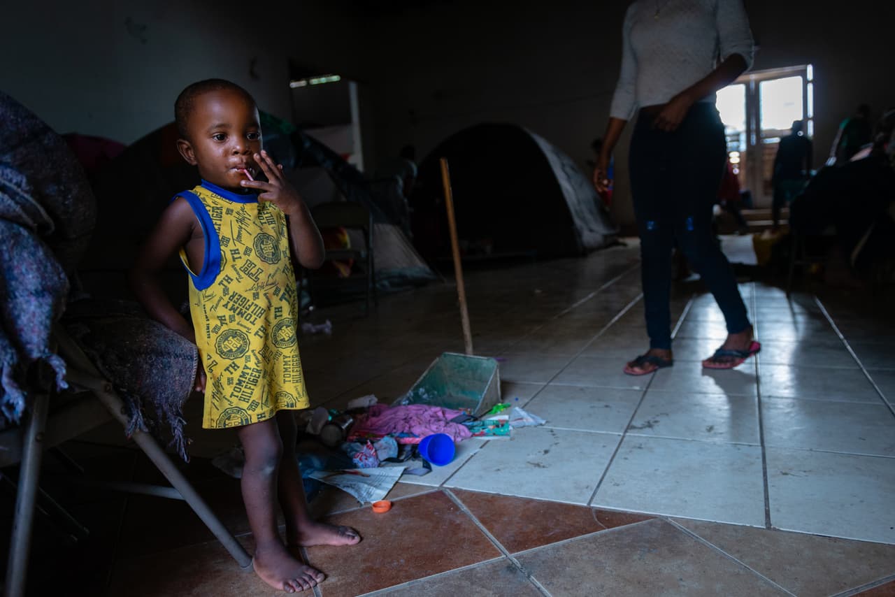 Adrian, el hijo de dos años de Pierre, quien lo mira desde el fondo. "Cuando tienes hijos, tienes que buscar un futuro mejor para ellos", dijo. Comparte una carpa con su familia y contó que dormir en un piso duro con algunas mantas es incómodo para ella. "Cuando eres un inmigrante y no estás trabajando es difícil comprar las cosas que necesitas" agregó. Cree que esperará en el refugio por al menos dos meses más antes de poder comparecer ante las autoridades de EEUU. "Nuestro número es 2,716".