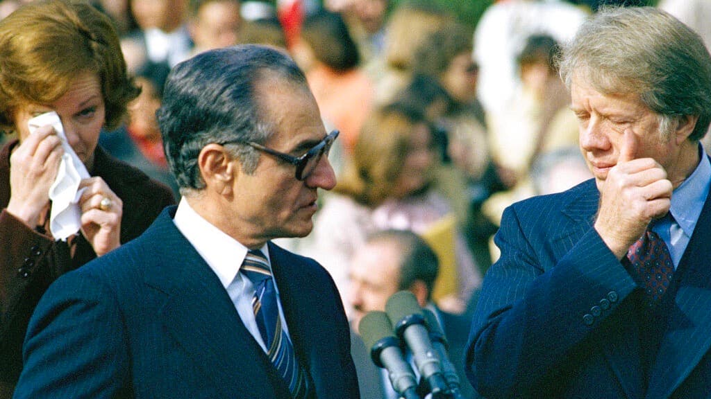 ARCHIVO - En esta foto de archivo del 15 de noviembre de 1977, la entonces primera dama Rosalyn Carter (izquierda), el sha Mohammad Reza Pahlavi (centro) y el entonces presidente estadounidense Jimmy Carter (derecha) reaccionan al gas lacrimógeno mientras manifestantes a favor y en contra del sha se enfrentan con la policía frente a la Casa Blanca durante una ceremonia. Decenas de personas resultaron heridas en la violencia. La toma de la embajada estadounidense en Teherán en 1979 terminó después de 444 días, pero tanto Estados Unidos como Irán siguen atrapados en una crisis que comenzó hace 40 años.