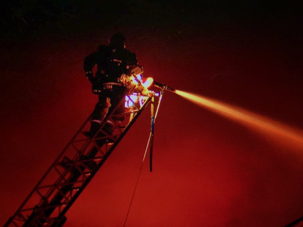 Un bombero trabaja en altura para echar agua dentro del almacén en llamas