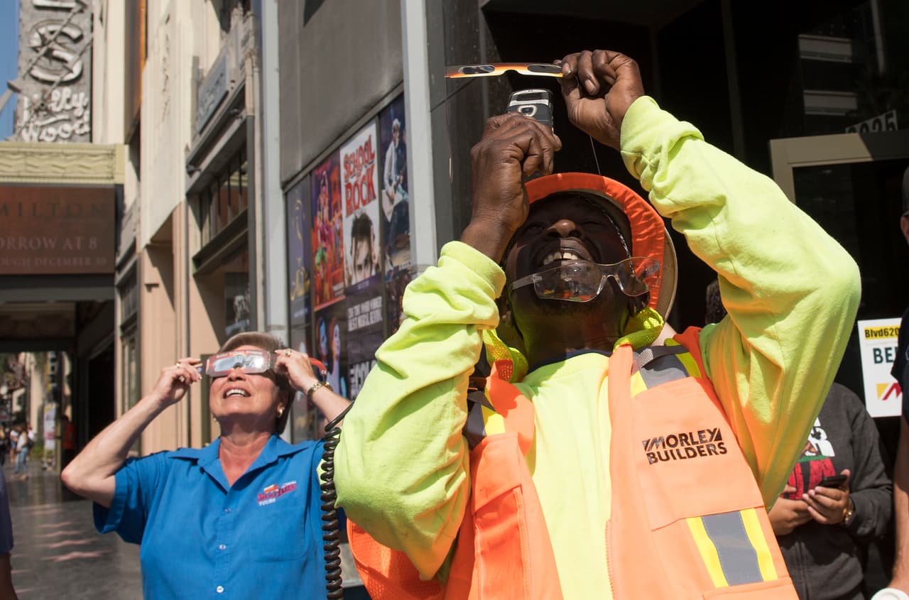 Un trabajador de la construcción toma fotos del eclipse con su celular en una calle de Los Ángeles.