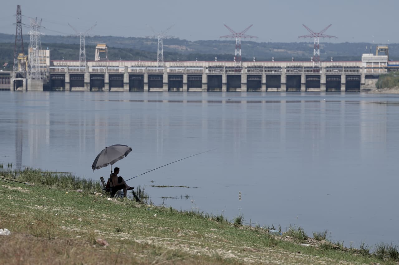 Un hombre pesca frente a Djerdap II, una gran presa en el río Danubio, entre Rumania y Serbia, cerca de Prahovo, Serbia, el martes 4 de agosto de 2026. (Foto AP/Darko Vojinovic)