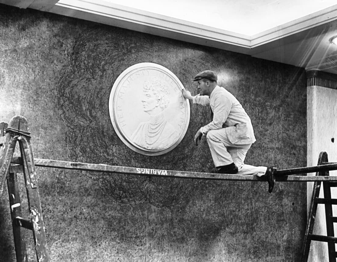 Con el apoyo financiero del gobierno británico la Cunard pudo reanudar el proyecto en 1934. Un obrero coloca en la pared la efigie de la reina Mary de Inglaterra, que dio nombre al buque.
