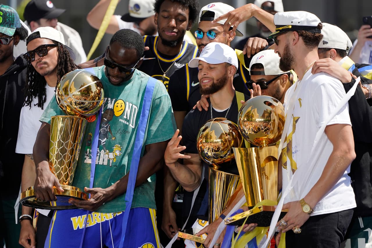 De izquierda a derecha, los Golden State Warriors, Draymond Green, Stephen Curry y Klay Thompson sostienen un trofeo mientras posan en el escenario antes del inicio de su desfile por el campeonato de la NBA en San Francisco, el lunes 20 de junio de 2022. (Foto AP/Eric Risberg)