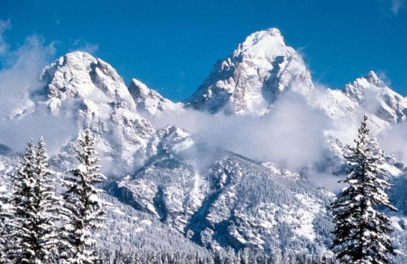 El Parque Nacional Grand Teton, ubicado en el noroeste de Wyoming, preserva un paisaje espectacular de montañas majestuosas, lagos prístinos y extraordinaria vida silvestre. El abrupto ascenso vertical de la silueta irregular de la cordillera Teton contrasta con la horizontalidad del valle cubierto de salvia y los lagos glaciales en su base, creando un paisaje mundialmente famoso que atrae a casi cuatro millones de visitantes por año.