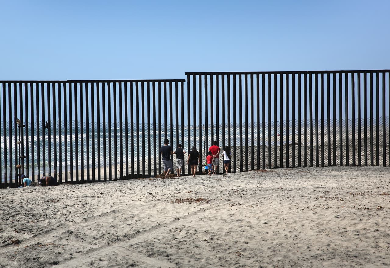 A group of Mexicans stare through the border fence where it meets the beach.