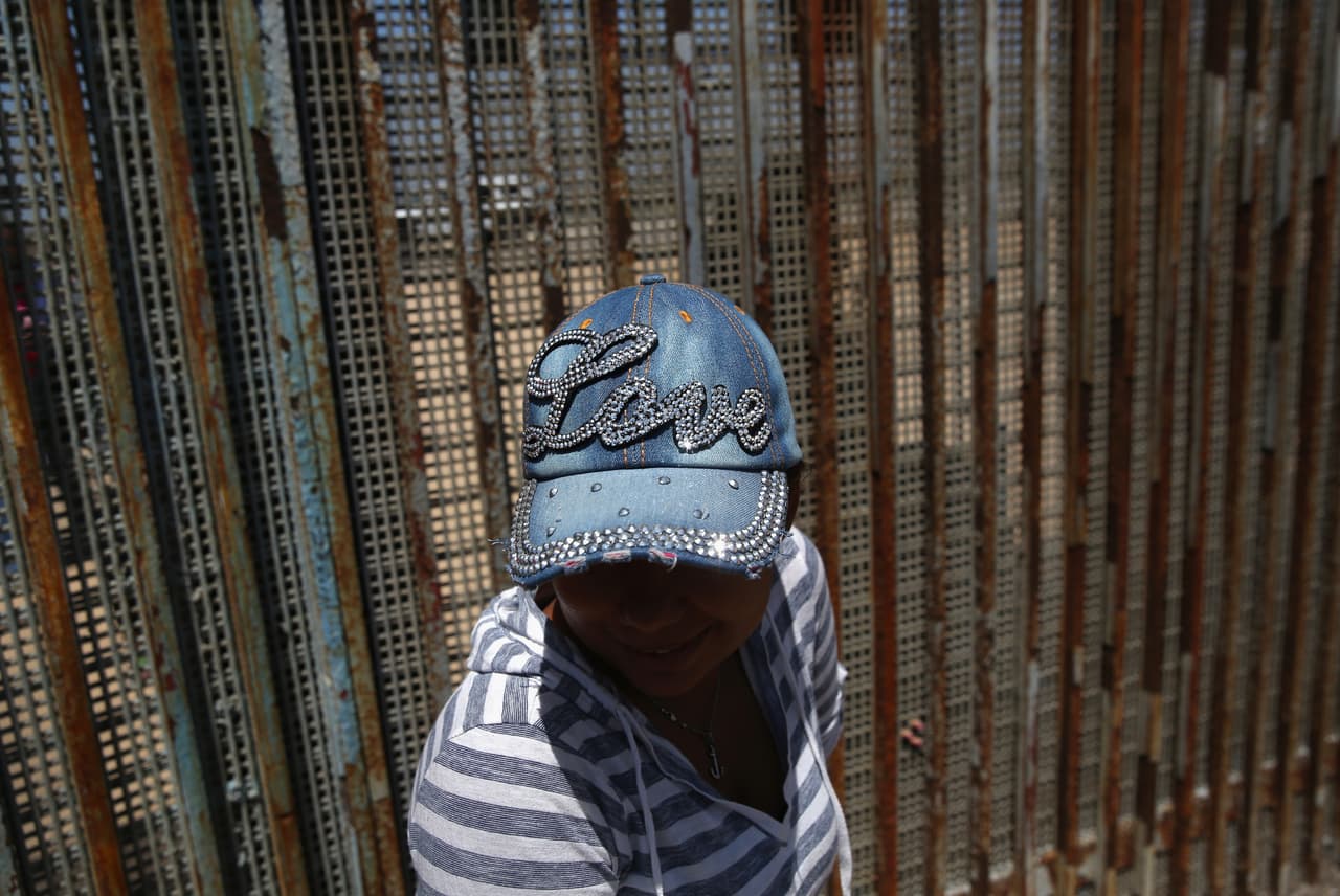 A woman take a pause while talking to relatives through the fence in Tijuana, May 1 2016.