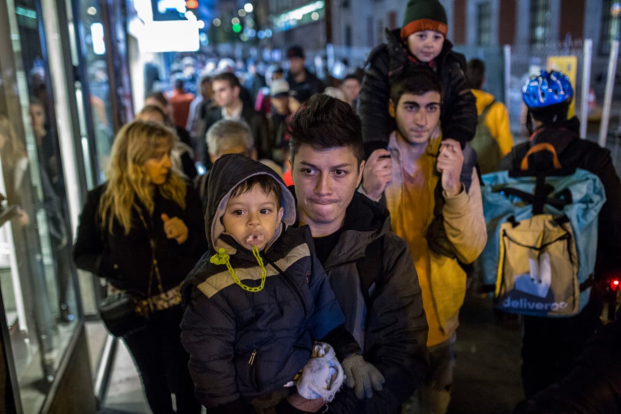 Federic and his son Mattias, from Colombia, along with dozens of migrants, walk down Calle Carretas de Madrid towards Parroquia San Carlos Borromeo.