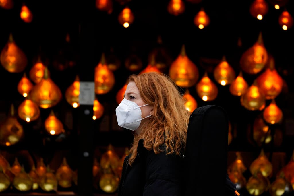 Una mujer utiliza una mascarilla mientras pasa entre luces navideñas en Londres.