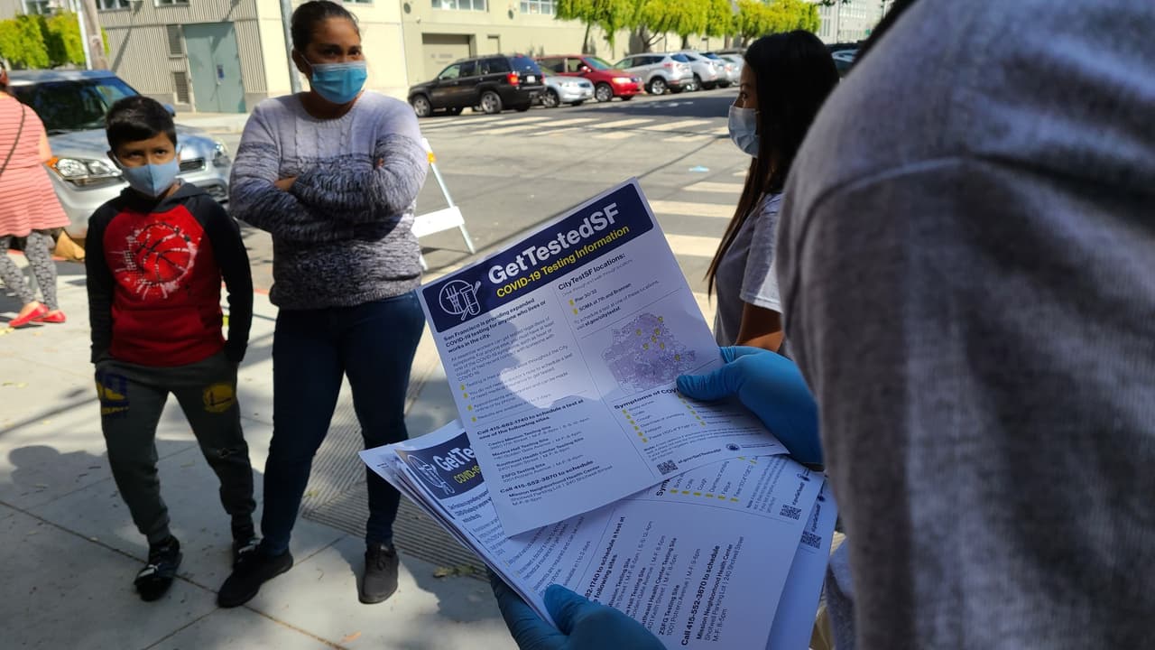 Miembros del 'Street Team' de UCSF otorgan volantes con información para hacerse la prueba de coronavirus gratuita en la fila de espera del Mission Food Hub.