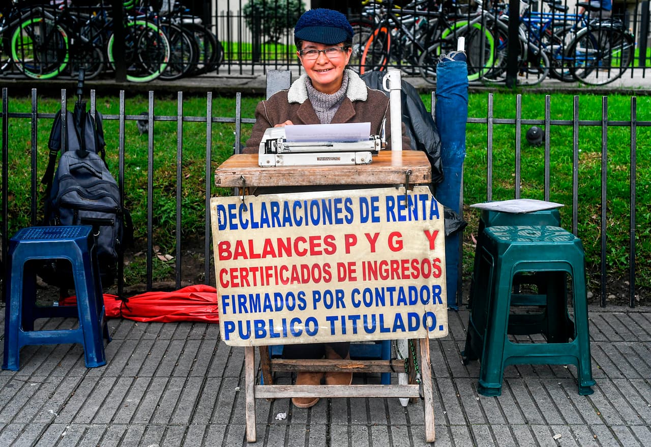 <b>Oficinista callejera, Colombia. </b> Candelaria Pinilla, de 63 años de edad, trabaja frente a la oficina distrital de impuestos en Bogotá. En puestos callejeros improvisados, estos expertos ayudan a sus clientes con los trámites burocráticos. Conocen mejor que nadie cómo llenar formularios, redactar documentos y escribir cartas en sus máquinas.