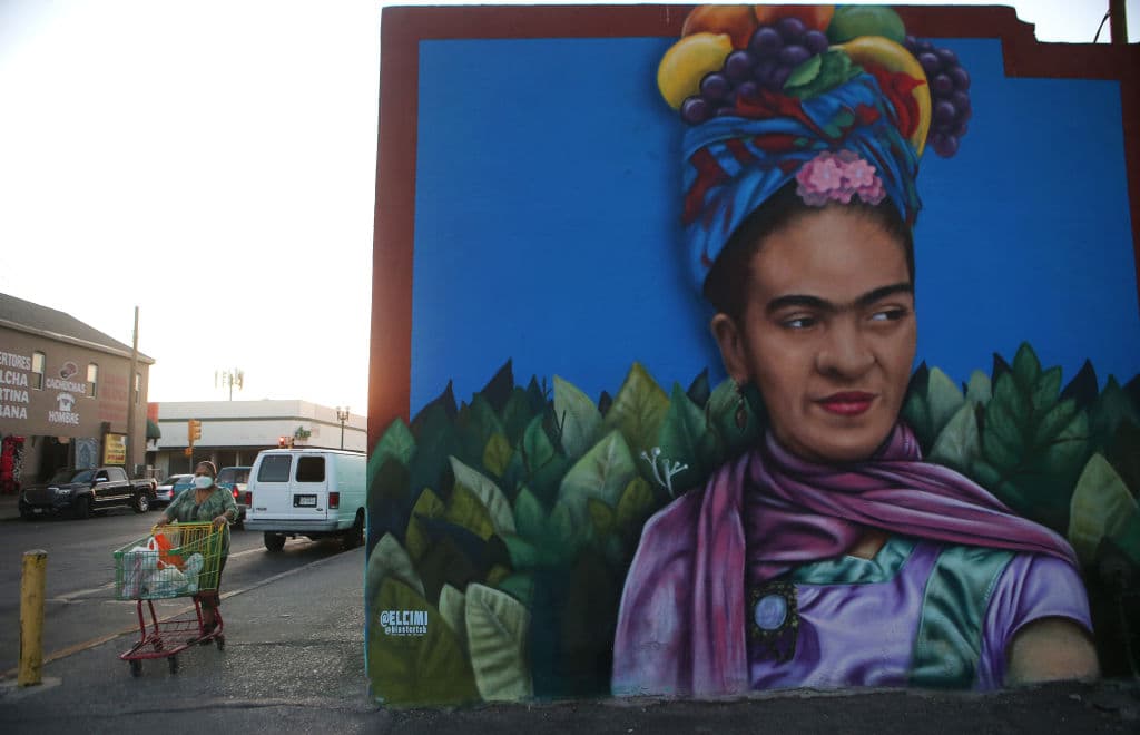 Una mujer con la cara cubierta camina junto a un mural de la pintora mexicana Frida Kahlo, obra del artista Jesús "CIMI" Alvarado en El Paso, de 800,000 habitantes. La emergencia en la ciudad fronteriza ha obligado a las autoridades a pedir ayuda al gobierno estatal y federal 
<a href="https://www.univision.com/local/san-antonio-kwex/elecciones-estados-unidos-2020/venga-y-mirelo-o-no-esta-el-horno-para-pavos-la-respuesta-de-un-artista-de-el-paso-a-un-polemica-tuit-de-ted-cruz" target="_blank">pues sus hospitales y morgues están rebasados</a>.