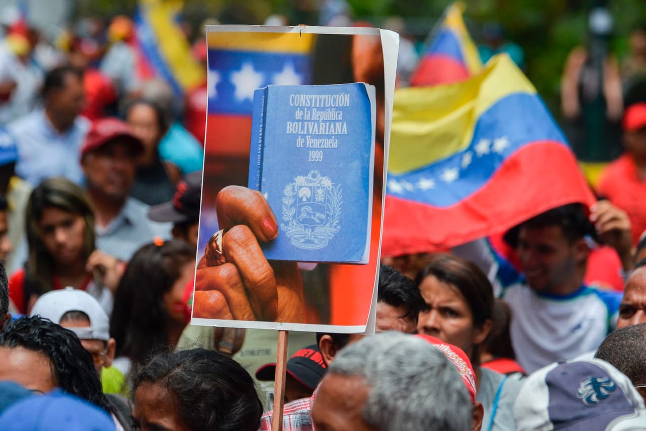 A supporter of Venezuelan President Nicolas Maduro holds a picture of the Constitution as he takes part in a rally in Caracas, on May 23, 2017, in which Maduro signed a document formally establishing the terms for electing members of a "constituent assembly" that will be tasked with drafting a new constitution Maduro formally launched moves to rewrite the constitution, defying opponents who accuse him of clinging to power in a political crisis that has sparked deadly unrest. His backers waved red, yellow and blue national flags in defiance of angry opposition protests after the death toll from weeks of clashes reached 53. But the opposition-controlled National Assembly promptly rejected Maduro's plan. / AFP PHOTO / LUIS ROBAYO (Photo credit should read LUIS ROBAYO/AFP/Getty Images)