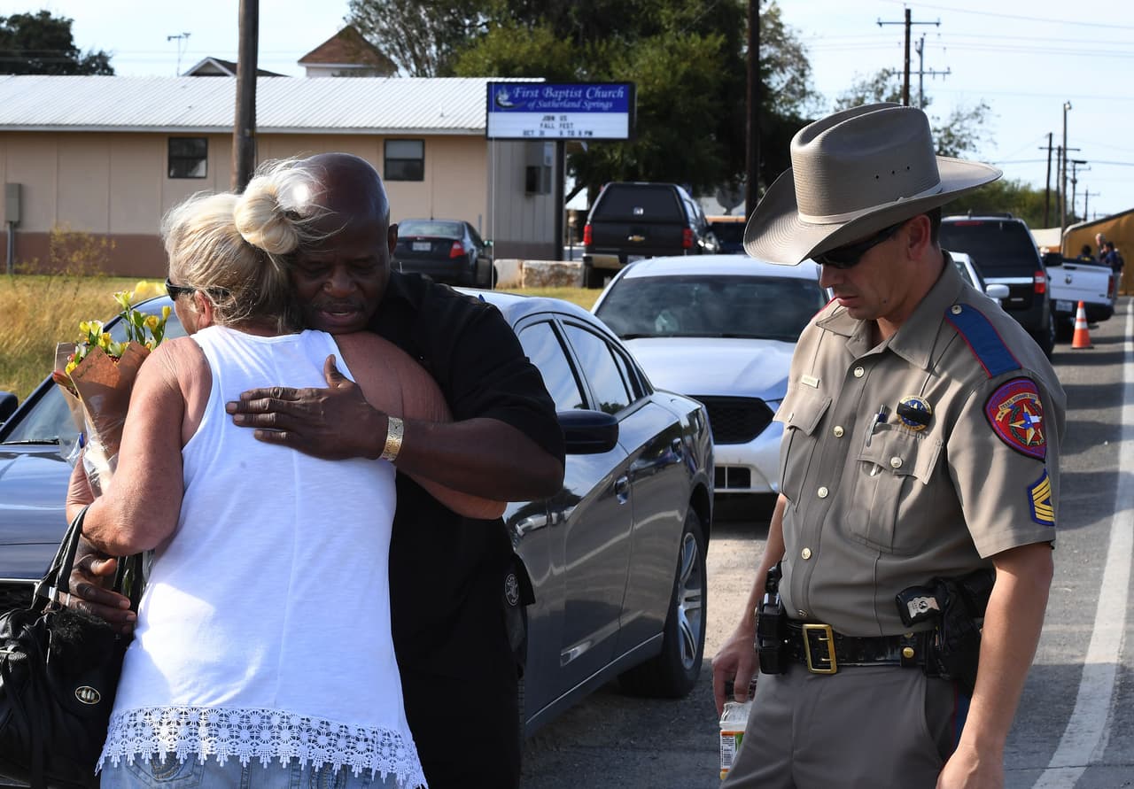 Local resident Jamie Rose (L) is hugged by church member Raymond Antonio as she delivers flowers, at the entrance to the First Baptist Church (back) after a mass shooting that killed 26 people in Sutherland Springs, Texas on November 6, 2017. A gunman wearing all black armed with an assault rifle opened fire on a small-town Texas church during Sunday morning services, killing 26 people and wounding 20 more in the last mass shooting to shock the United States. / AFP PHOTO / Mark RALSTON (Photo credit should read MARK RALSTON/AFP/Getty Images)