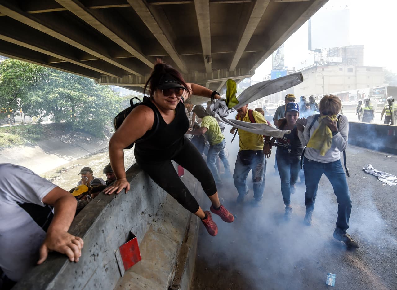 Opponents of Nicolás Maduro's regime flee from tear gas launched by the police, next to the Guaire River's dirty waters. April 19, 2017.