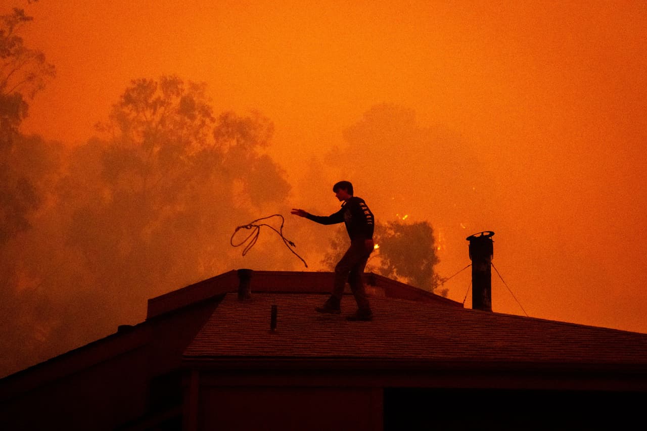 Sage Harvey arroja una cuerda por el tejado de su casa mientras las llamas del incendio Plaskett se acercan, el 28 de agosto de 2026, en Big Sur, California. (AP Foto/Ethan Swope)
