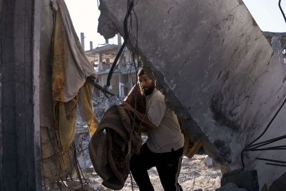 Un palestino lleva una alfombra a las ruinas de su casa.