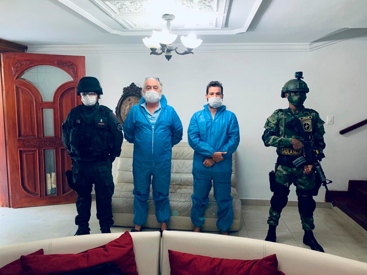En esta fotografía proporcionada por la fiscalía de Colombia, un agente de la policía y un soldado flanquean a Mark Grenon (segundo desde la izquierda) y a su hijo Joseph Grenon, durante un registro en Santa Marta, Colombia, el martes 11 de agosto de 2020. (Fiscalía General de Colombia vía AP)