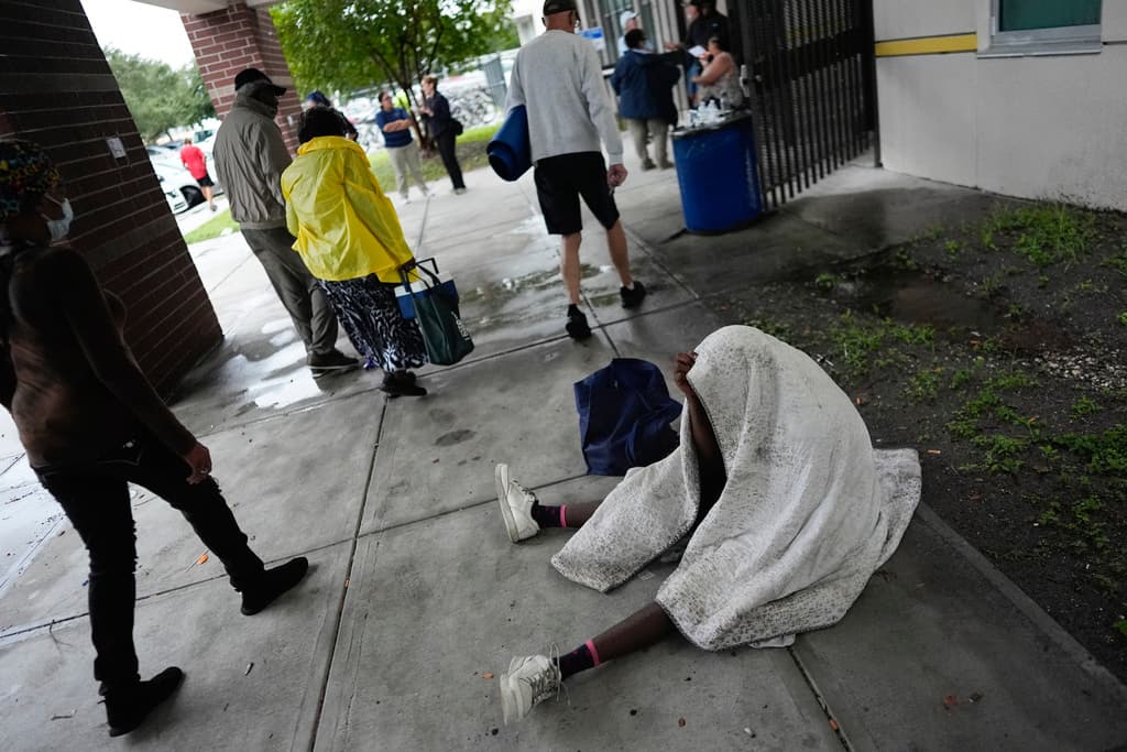 <b>Descansa en la acera:</b> Un hombre descansa mientras otros llevan suministros a la escuela secundaria Gibbs, un refugio gubernamental contra tormentas donde 1,700 personas ya habían buscado refugio a última hora de la mañana, antes de la llegada del huracán Milton, en St. Petersburg, Florida, el miércoles 9 de octubre de 2024. (Foto AP/Rebecca Blackwell)