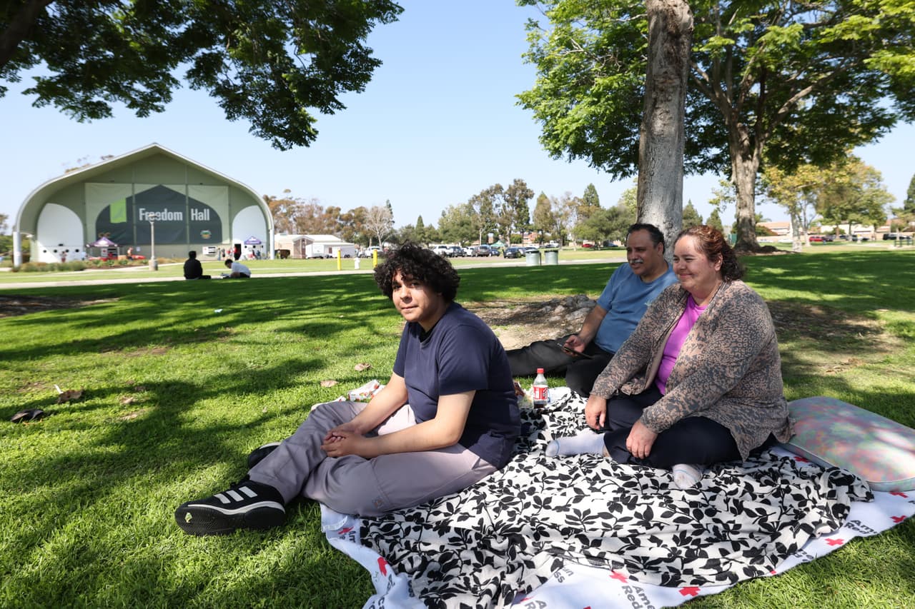 De izquierda a derecha, Francisco López Jr., su padre, Francisco Sr., y su madre, Irma Ramírez, esperan afuera información después de pasar la noche en Freedom Hall, un centro de evacuación en Fountain Valley, California, el sábado 23 de mayo de 2026. (Foto AP/Jill Connelly)