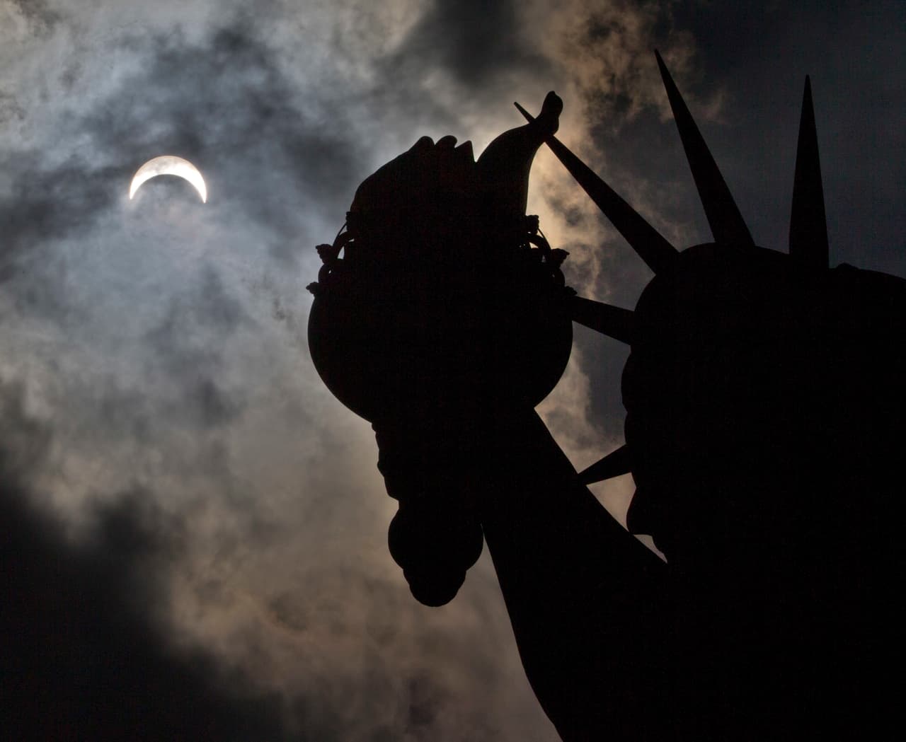 El sol y la luna entre las nubes, sobre la silueta de la estatua de la Libertad en la Gran Manzana.