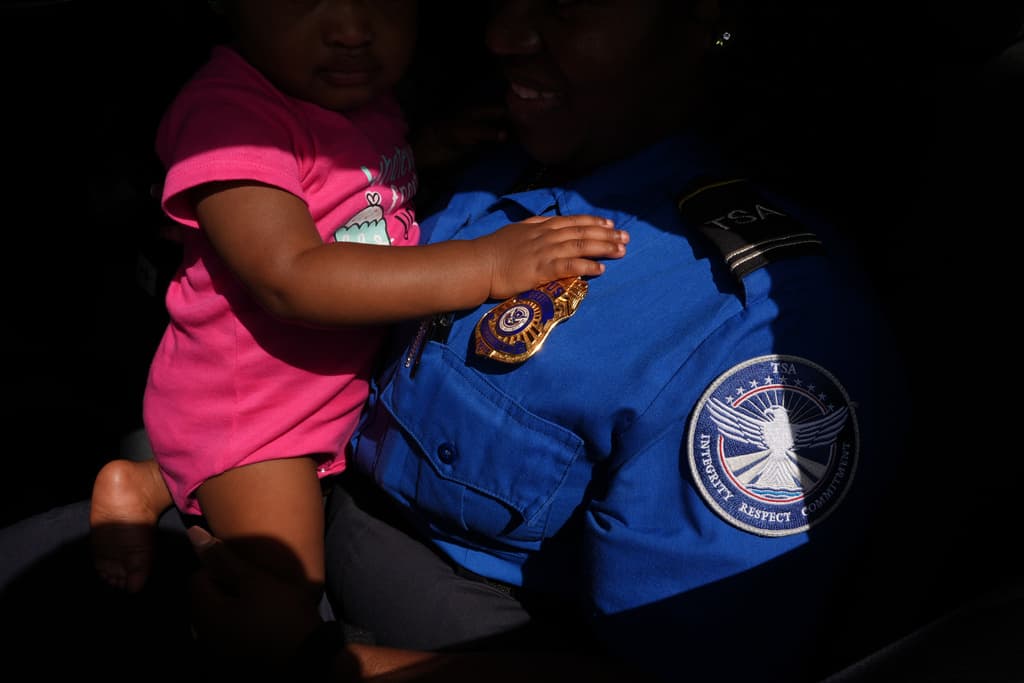 La agente de la TSA Sashene McLean, con su hija de un año en brazos, llega del trabajo para recoger una donación de productos, carne y yogurt en un centro de distribución de alimentos organizado para ayudar a empleados federales sin pago durante el cierre del gobierno en Dania Beach, Florida, el 28 de octubre de 2025.